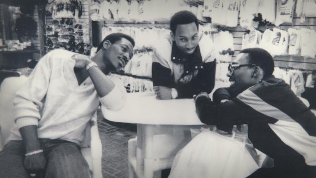 A black and white image of three men leaning on a table.
