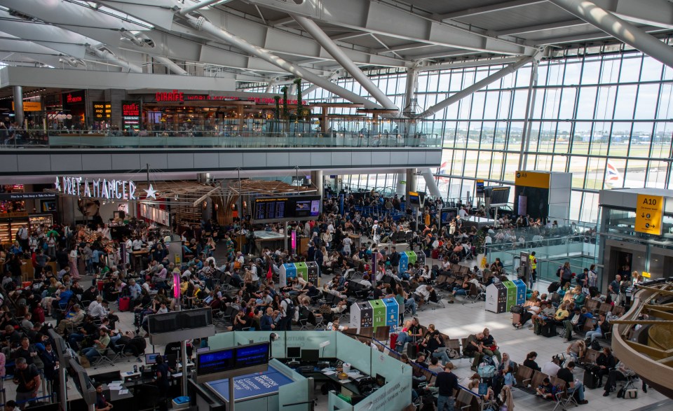 An overhead shot of a very busy Heathrow Airport, showing the large, modern interior of the airport with many people sitting and walking, and an airplane visible through the windows.