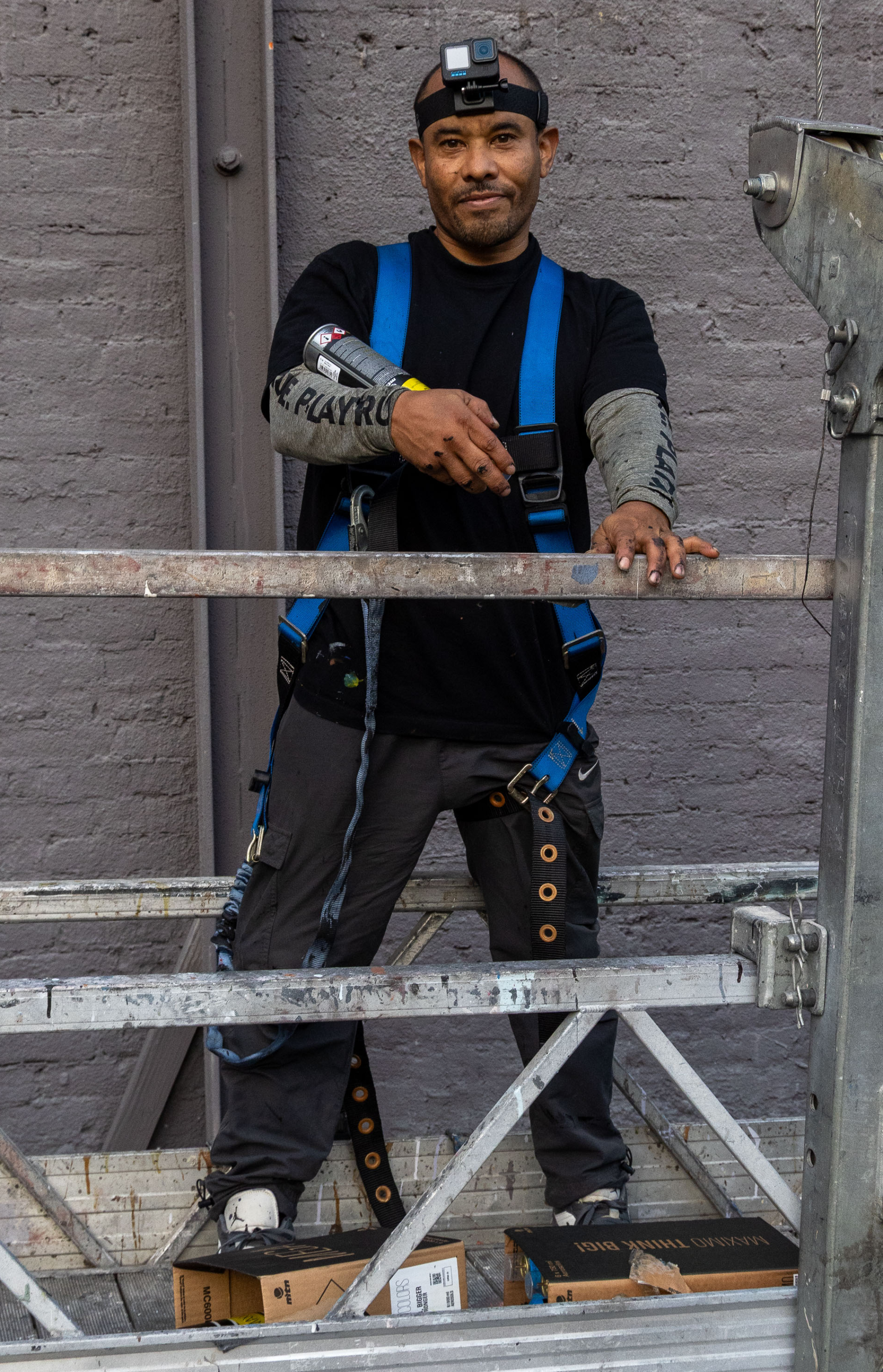 Daniel 'Chaka' Ramos stands on a scaffold, holding a can of spray paint and wearing a blue harness and black headlamp.