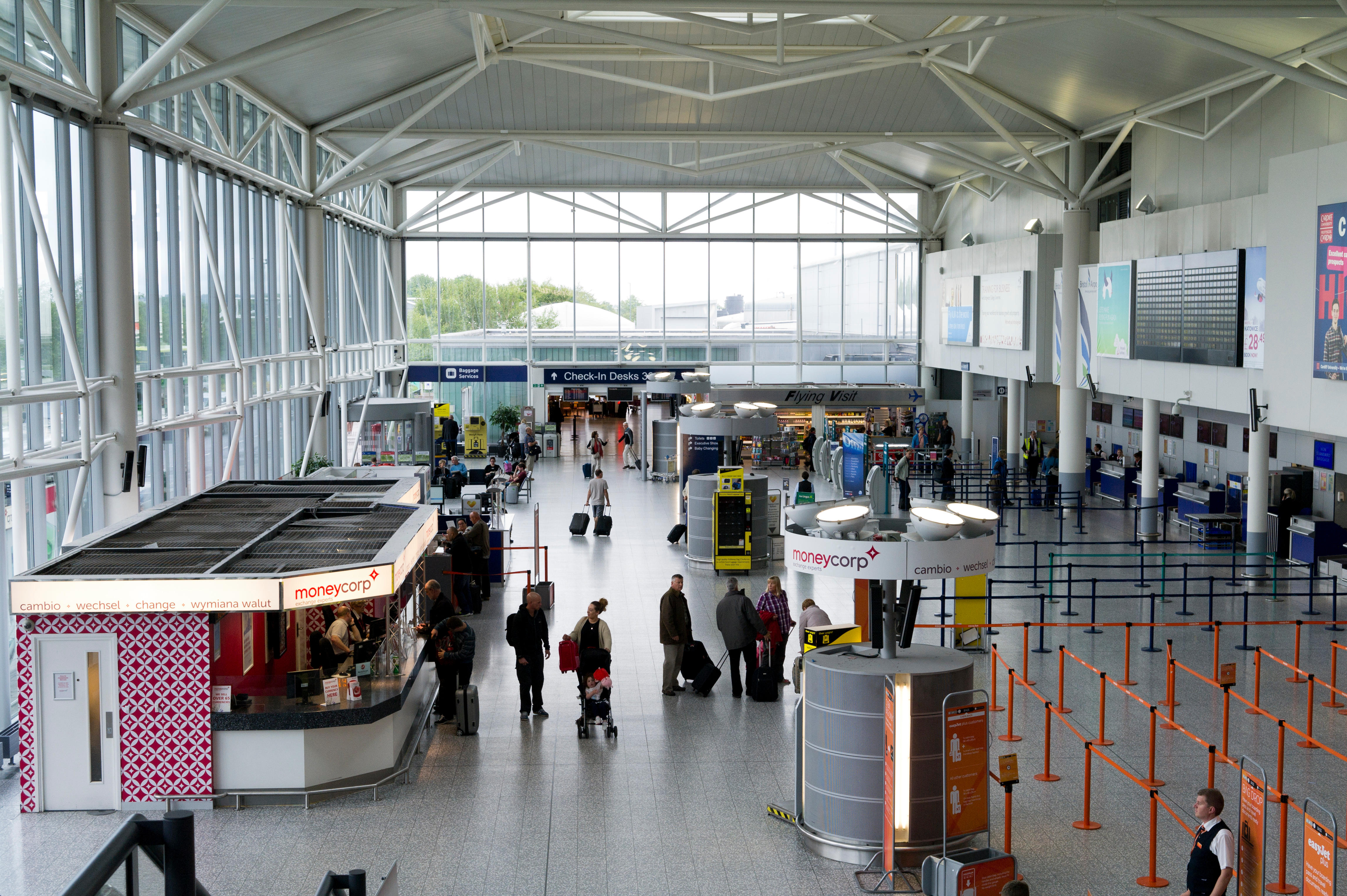 Interior of Bristol Airport showing various people, a Moneycorp currency exchange kiosk, and check-in desks.