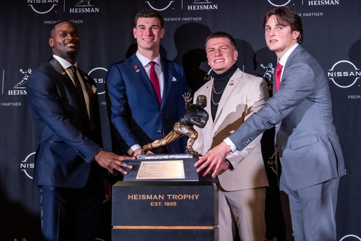 All four 2025 Heisman Trophy finalists pose with a hand on the trophy before the award ceremony