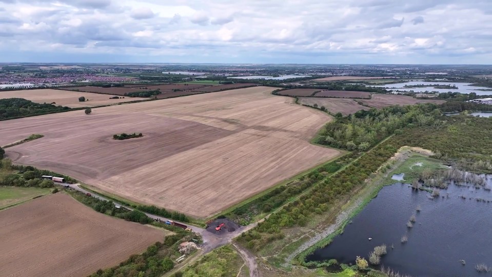 An aerial photo of brown fields, lakes, a road, and distant towns under a cloudy sky.