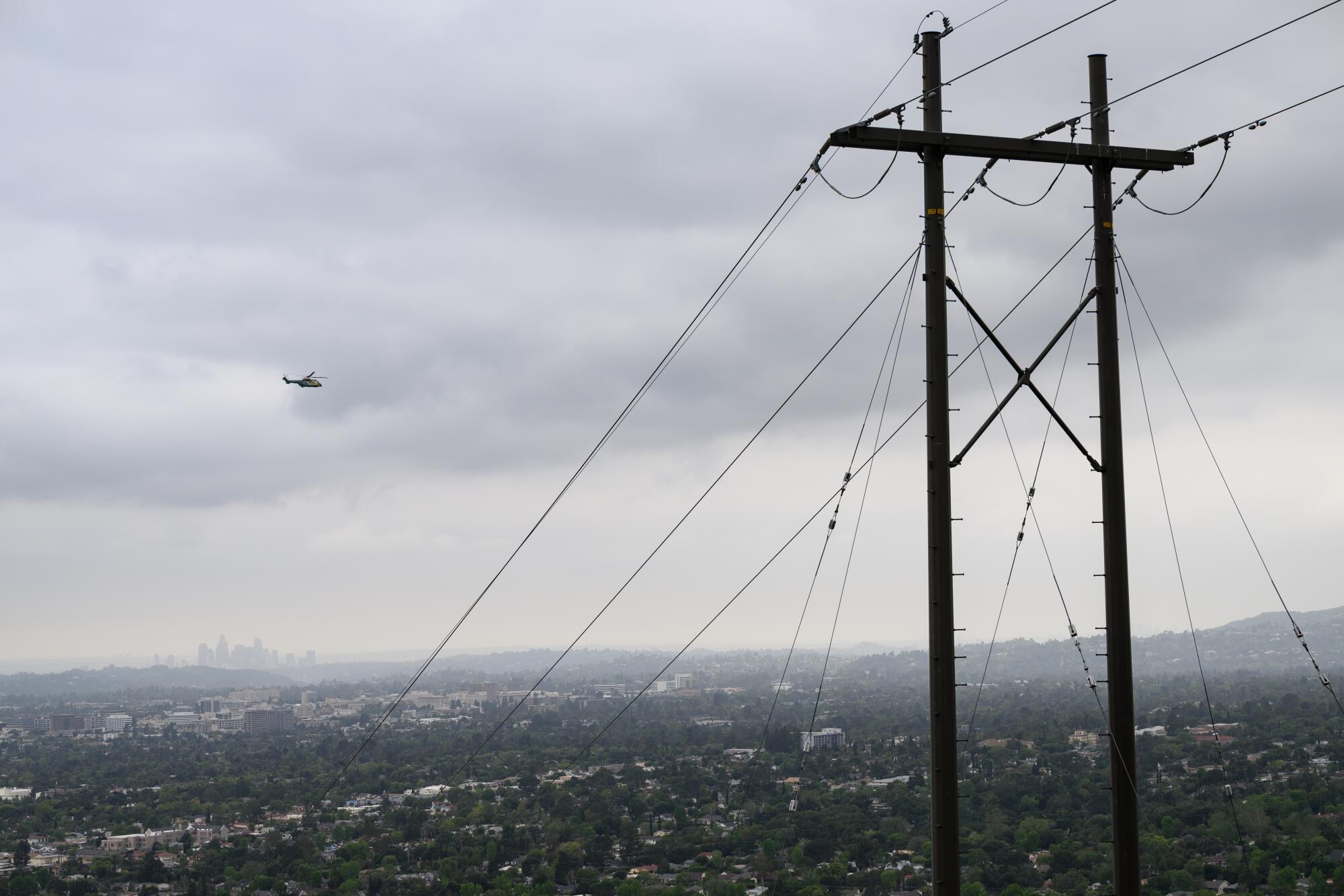 A helicopter flies over the downtown Los Angeles skyline during a cloudy day