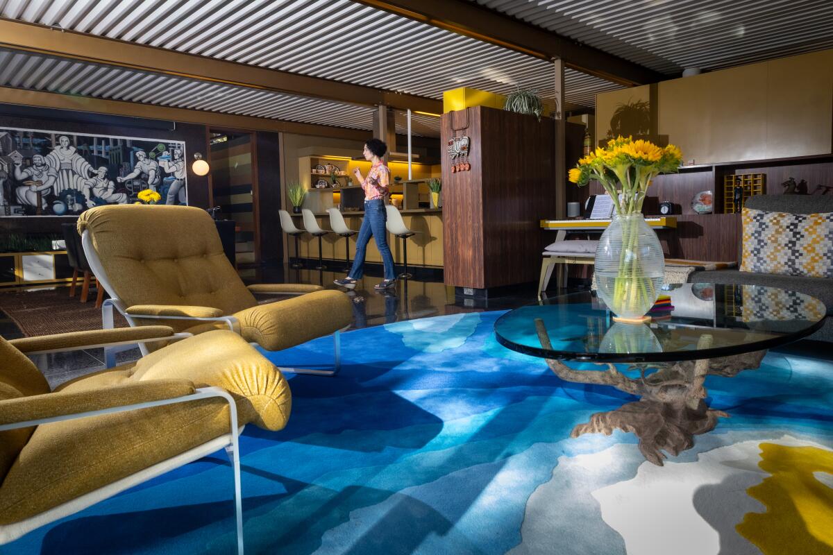 Linda Brettler walks through a living room with a blue carpet.