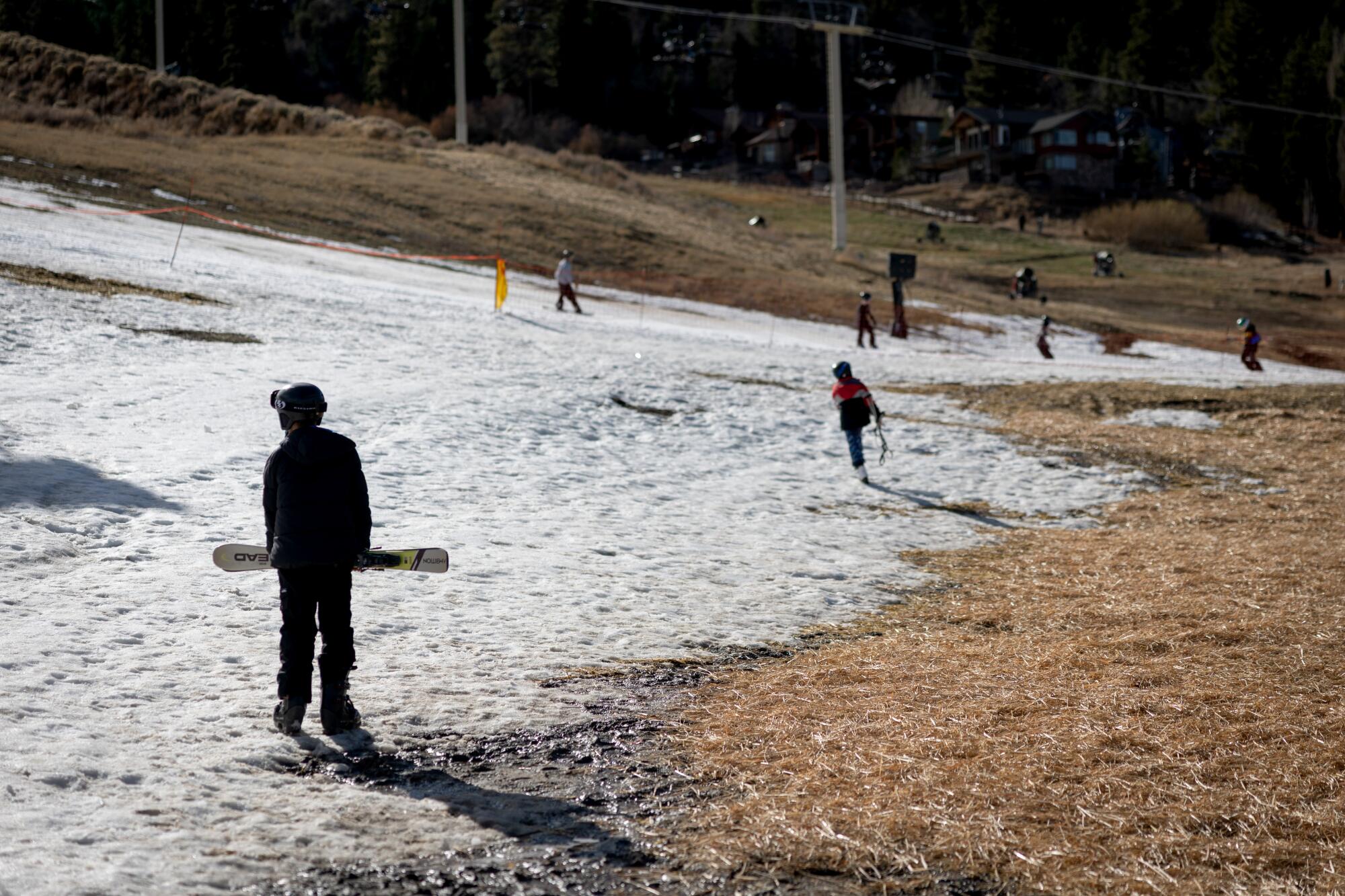 Skiers and snowboarders navigate bare areas next to snowy ground at Big Bear Mountain Resort.