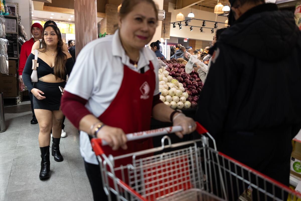 A woman in a night dress walks behind a lady pushing a cart.