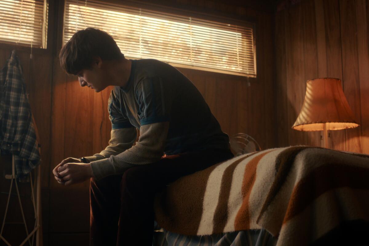 A teenage boy looks forlorn while sitting on a bed.