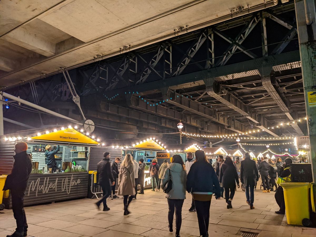People browsing the busy Christmas Market under Hungerford Bridge and Golden Jubilee Bridges in Southbank at night