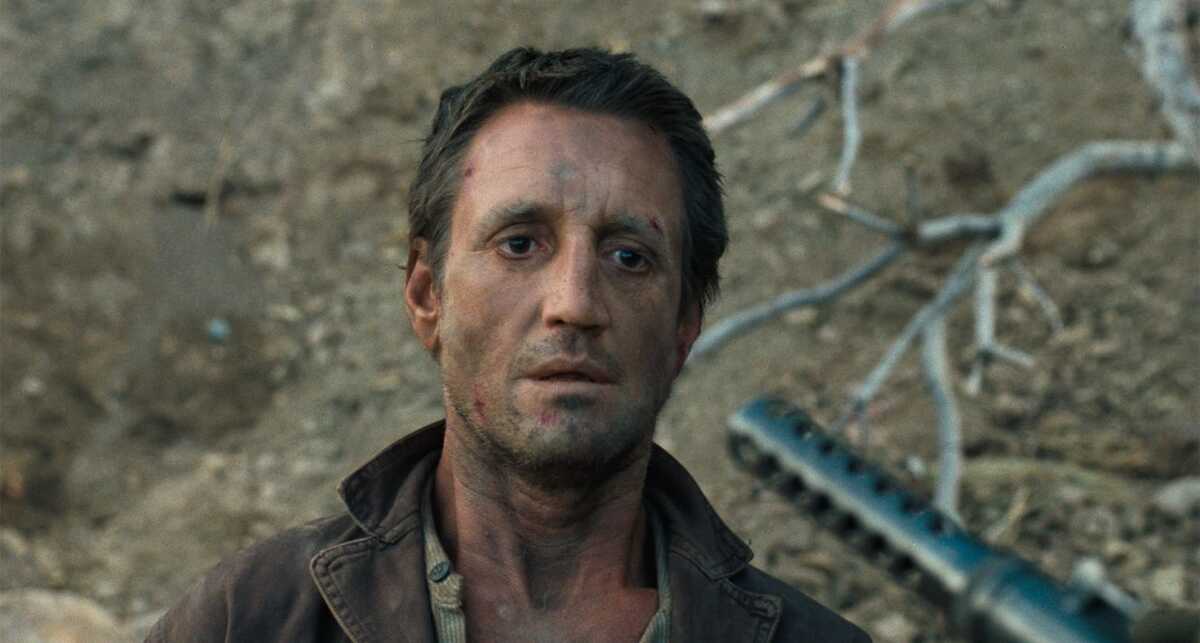 A man stands still with a rifle pointed at him.