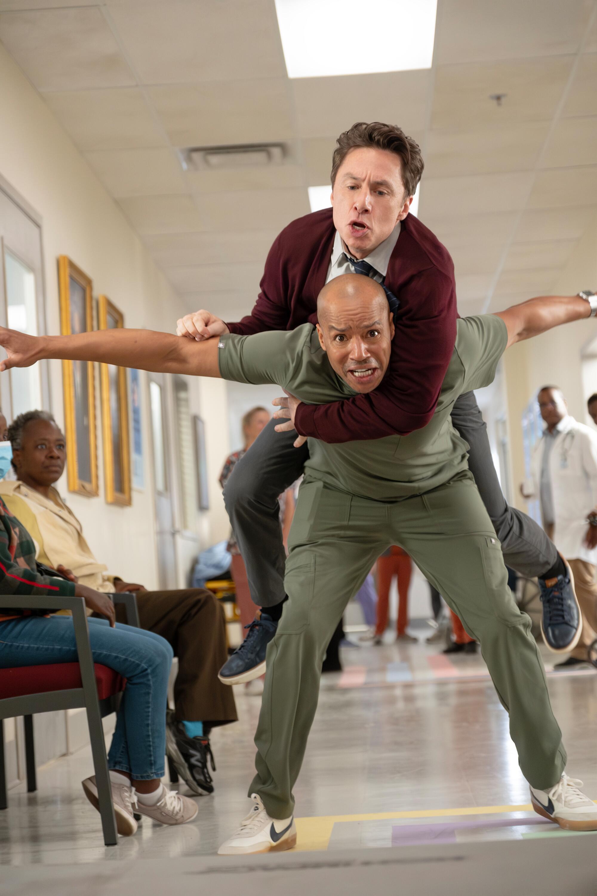 Zach Braff is balanced on the back of Donald Faison, who has his arms out like airplane wings