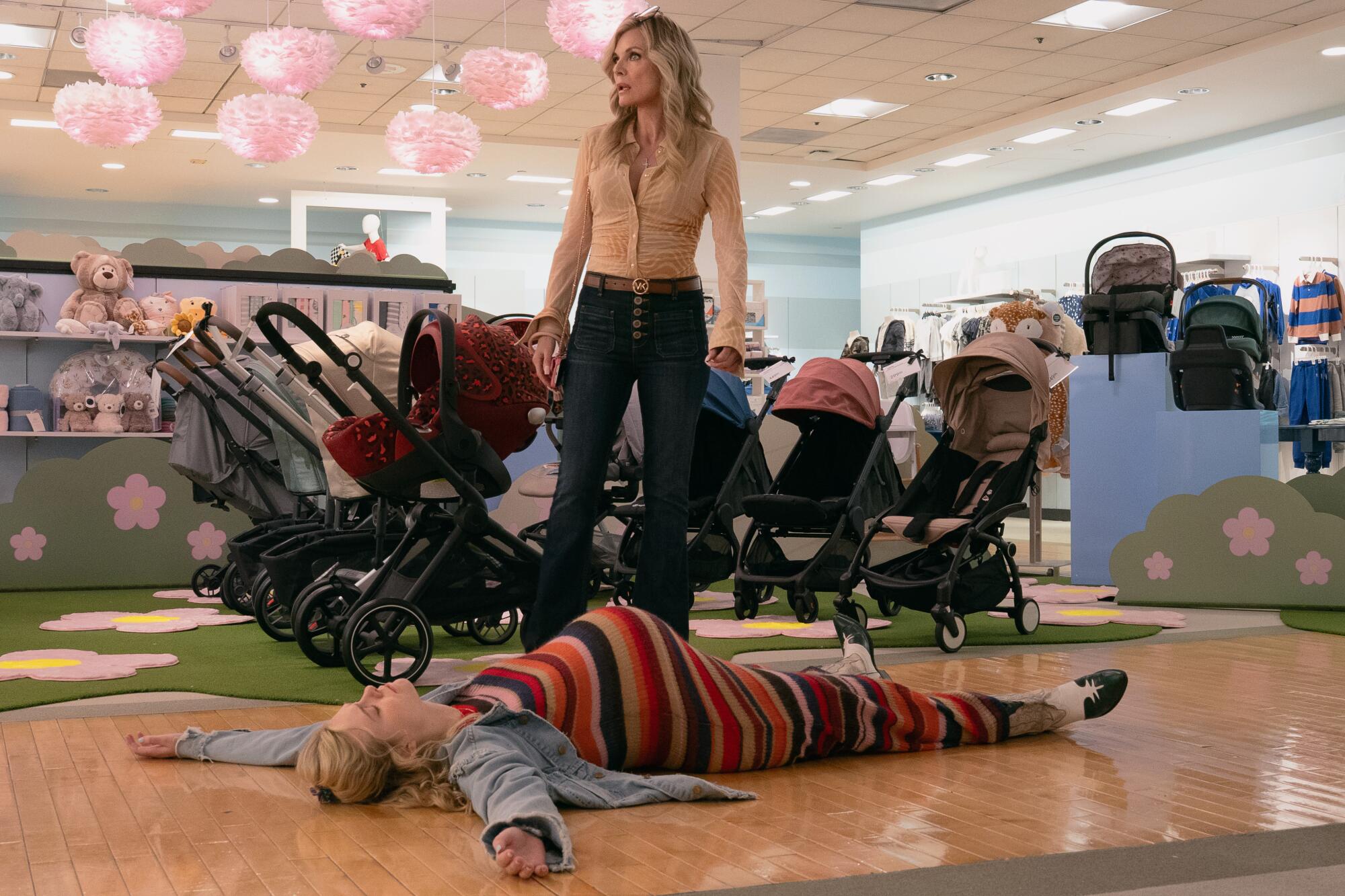 A woman stands near a row of baby strollers as a pregnant woman lies on the floor.