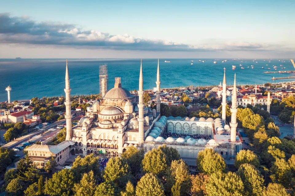 Sunrise drone photo of the Blue Mosque, showing its domes and minarets, with the sea and many ships in the background.