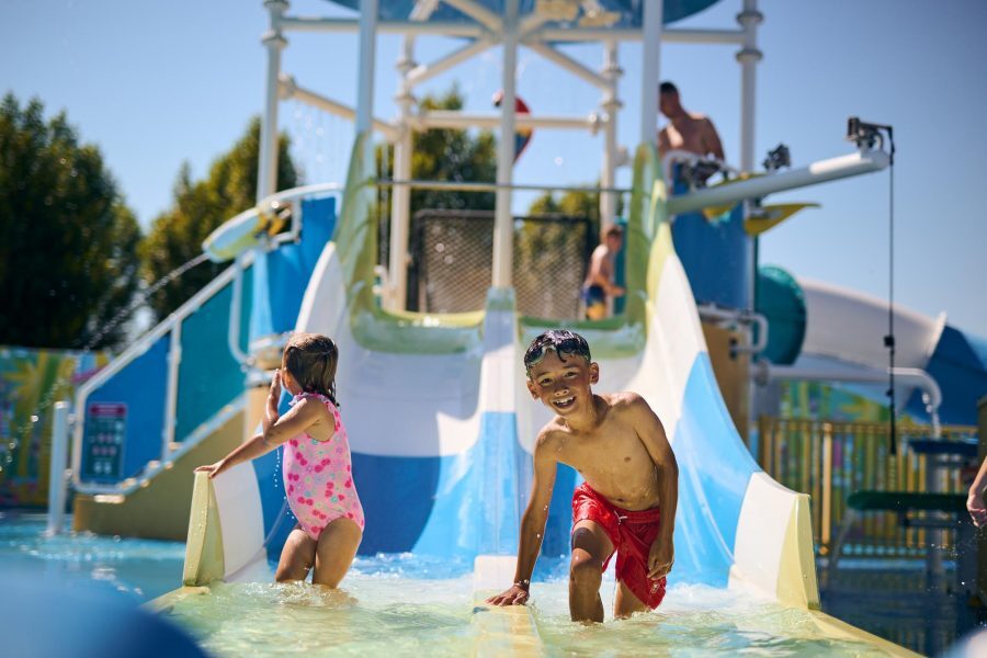 A boy and a girl playing in a water park, with blue and white water slides in the background.
