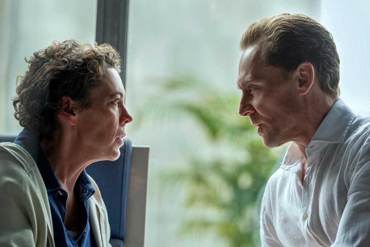 A woman in a blue shirt and light colored hoodie looks intently at a man in a white shirt sitting across from her.