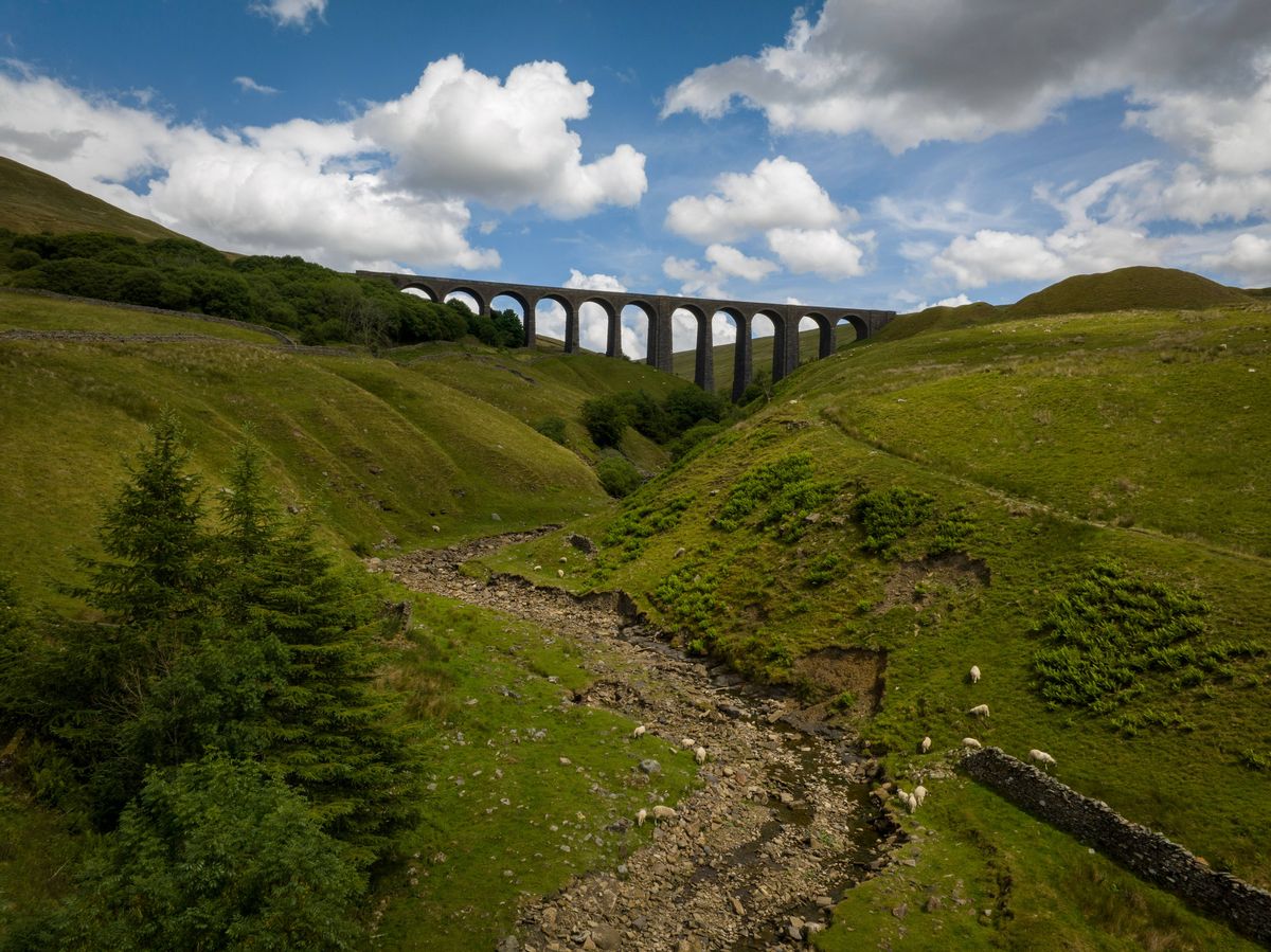 An aerial photograph of the famous Arten Gill Railway Viaduct on the border of the Yorkshire Dales and Cumbria, in England. The photograph was produced on a bright summers day with blue skies and rolling white clouds.