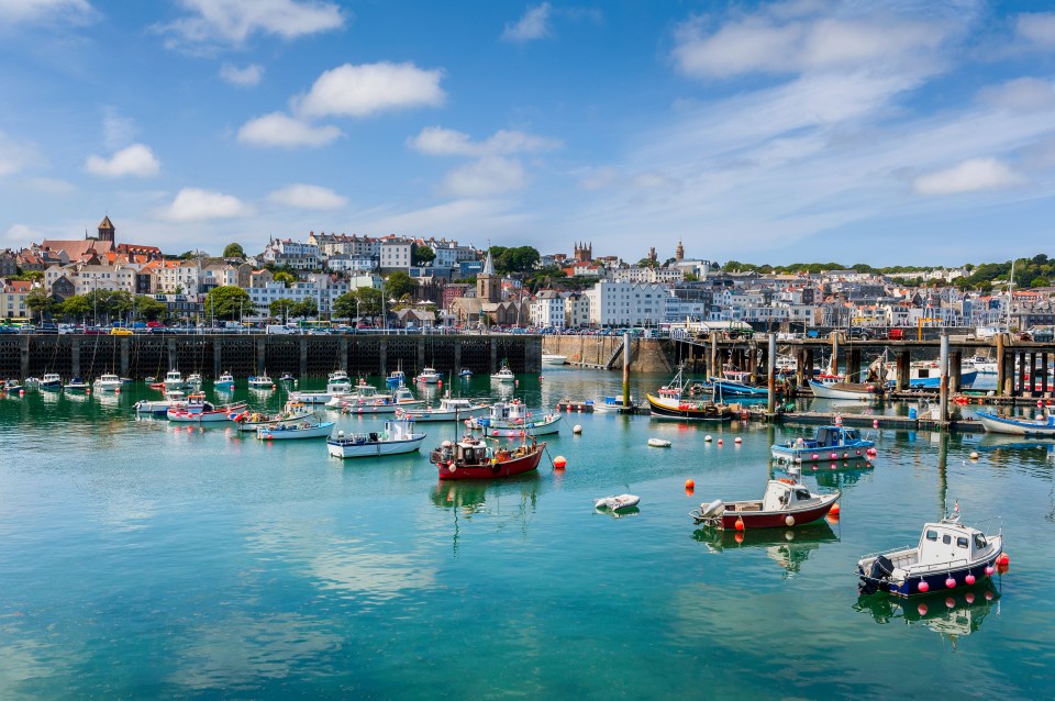 Harbour and skyline of Saint Peter Port, Guernsey, with many boats docked in the water and buildings on the hill.