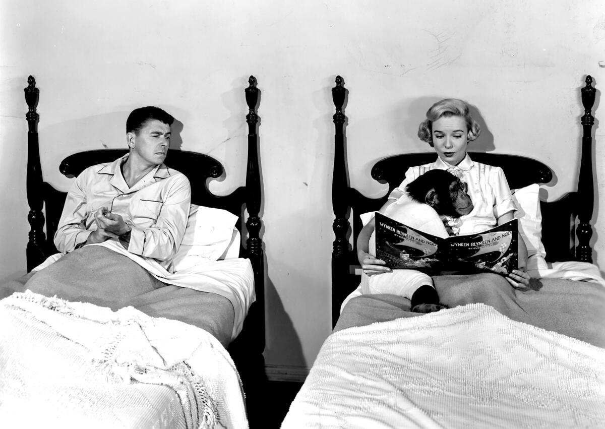 A black-and-white image of a man and a woman cradling a monkey sitting upright in separate twin beds.