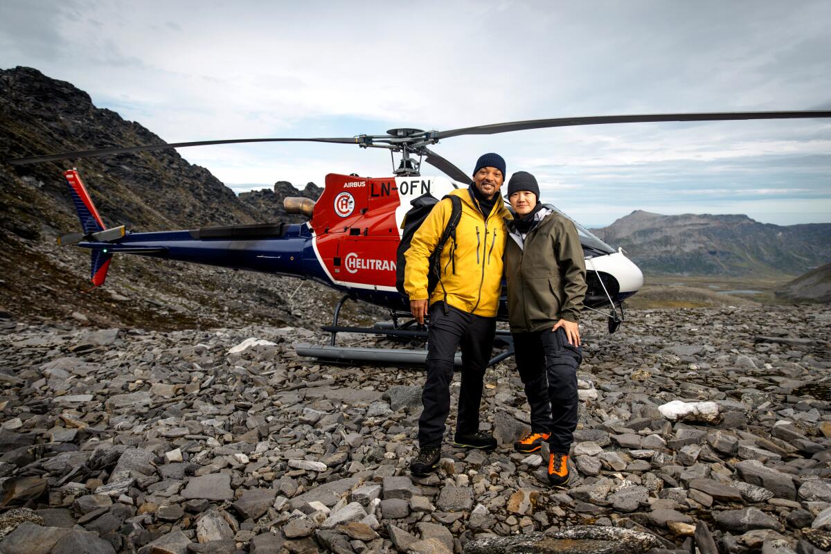 Two people stand in front of a grounded helicopter 