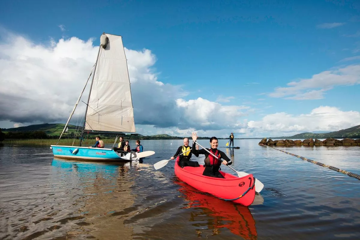Individuals are engaging in recreational boating activities on a serene body of water, with a striking structure visible in the background under a clear sky.
