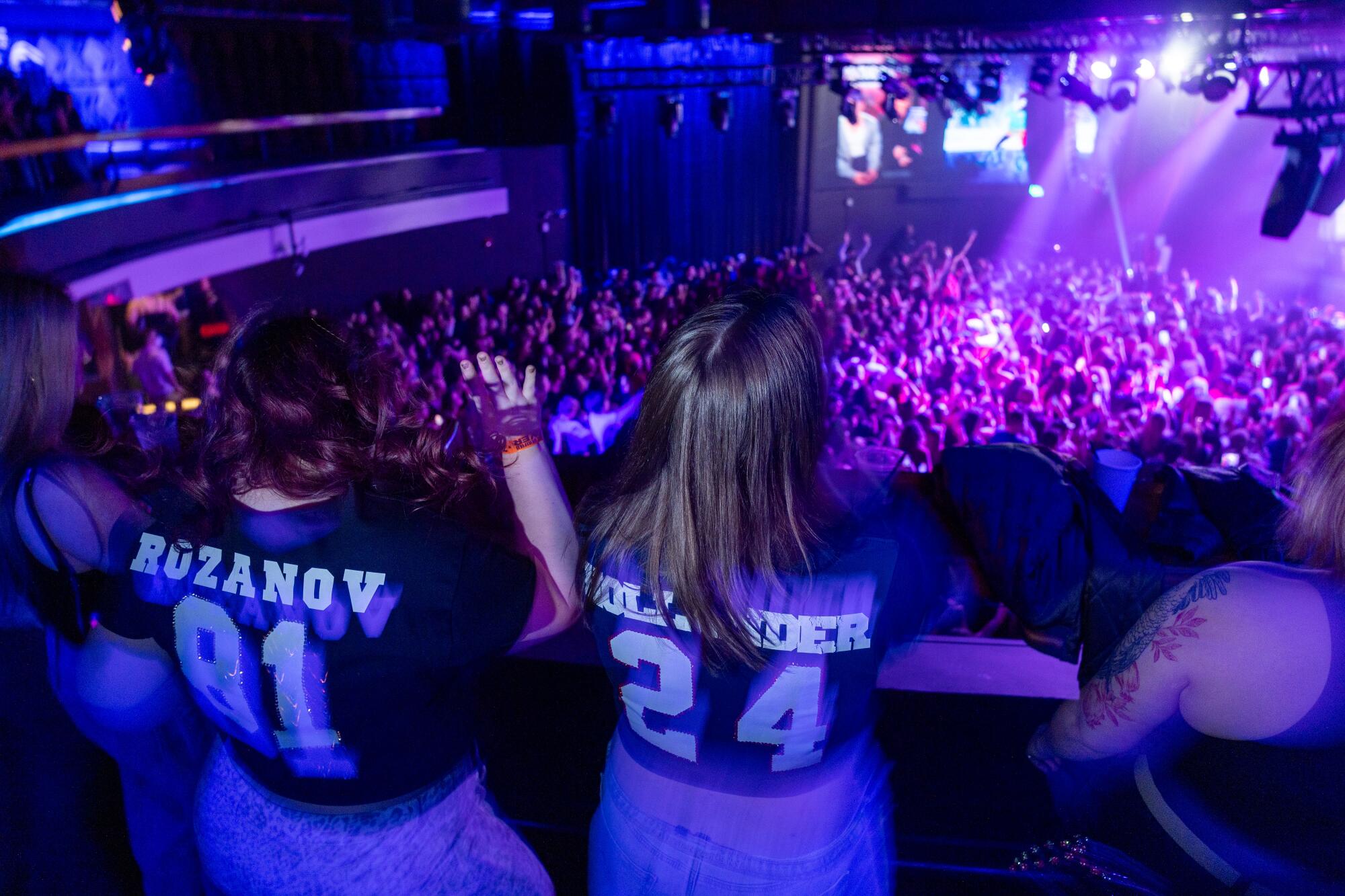 Two people wearing hockey jersey with Rozanov and Hollander on the back, look down at a big crowd from a balcony.