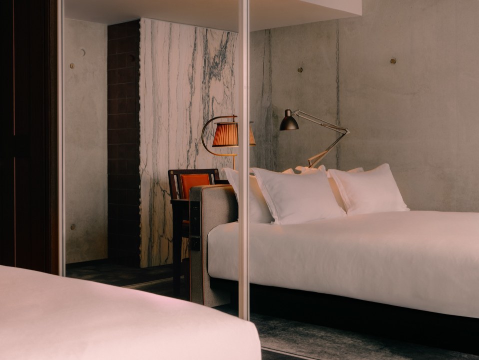 A modern bedroom with a bed and a reflected armchair and lamps in a mirror.
