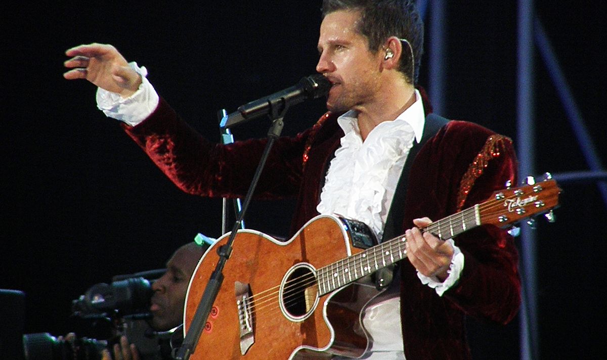 A man holding a guitar sings into a microphone on stage