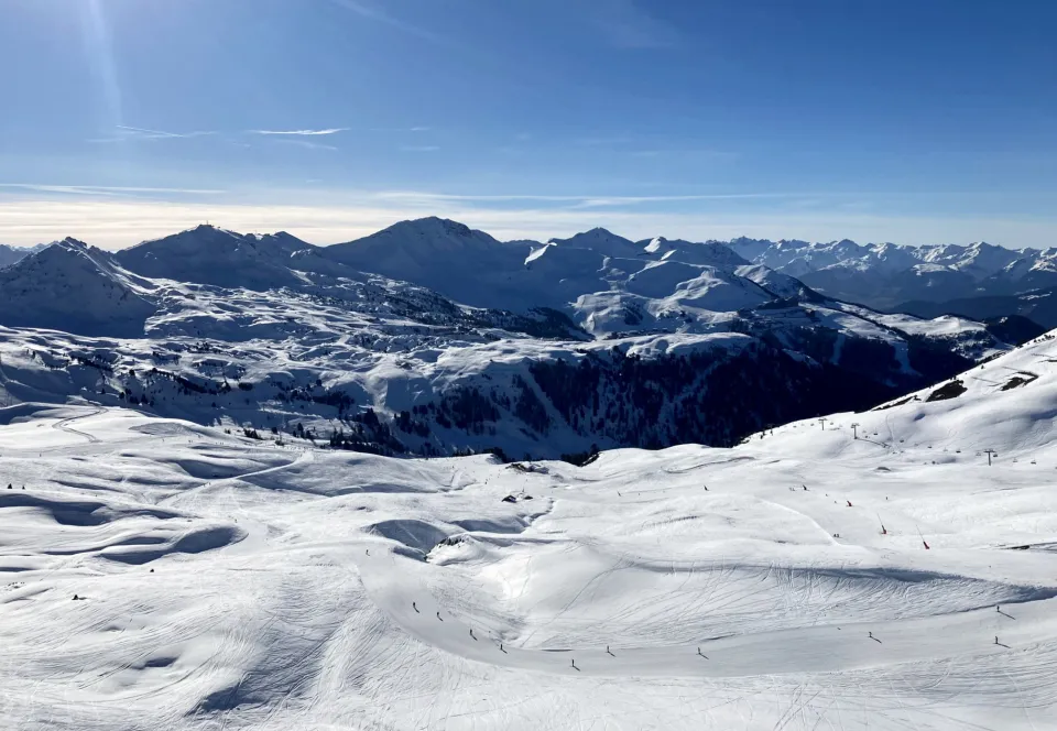 Skiers on the slopes of La Plagne, France, with snow-covered mountains in the background.