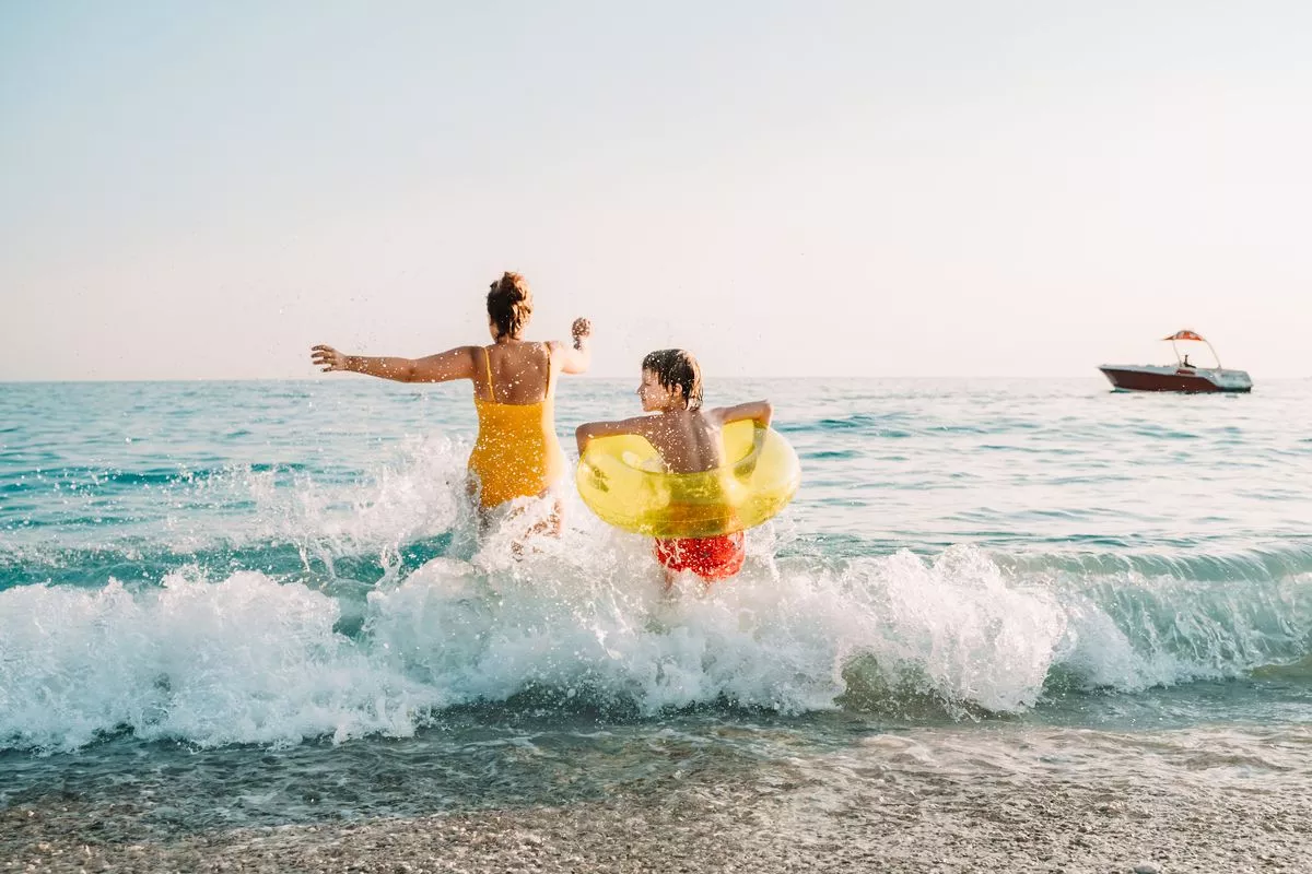 Young mother with little son runs into the sea on sunset light
