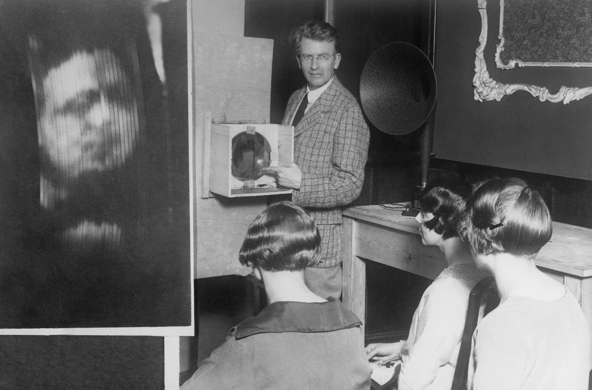 John Logie Baird demonstrates his "televisor", a receiver for a mechanical system of television transmission involving a spinning disk. The system was soon overtaken by electronic television after World War II.