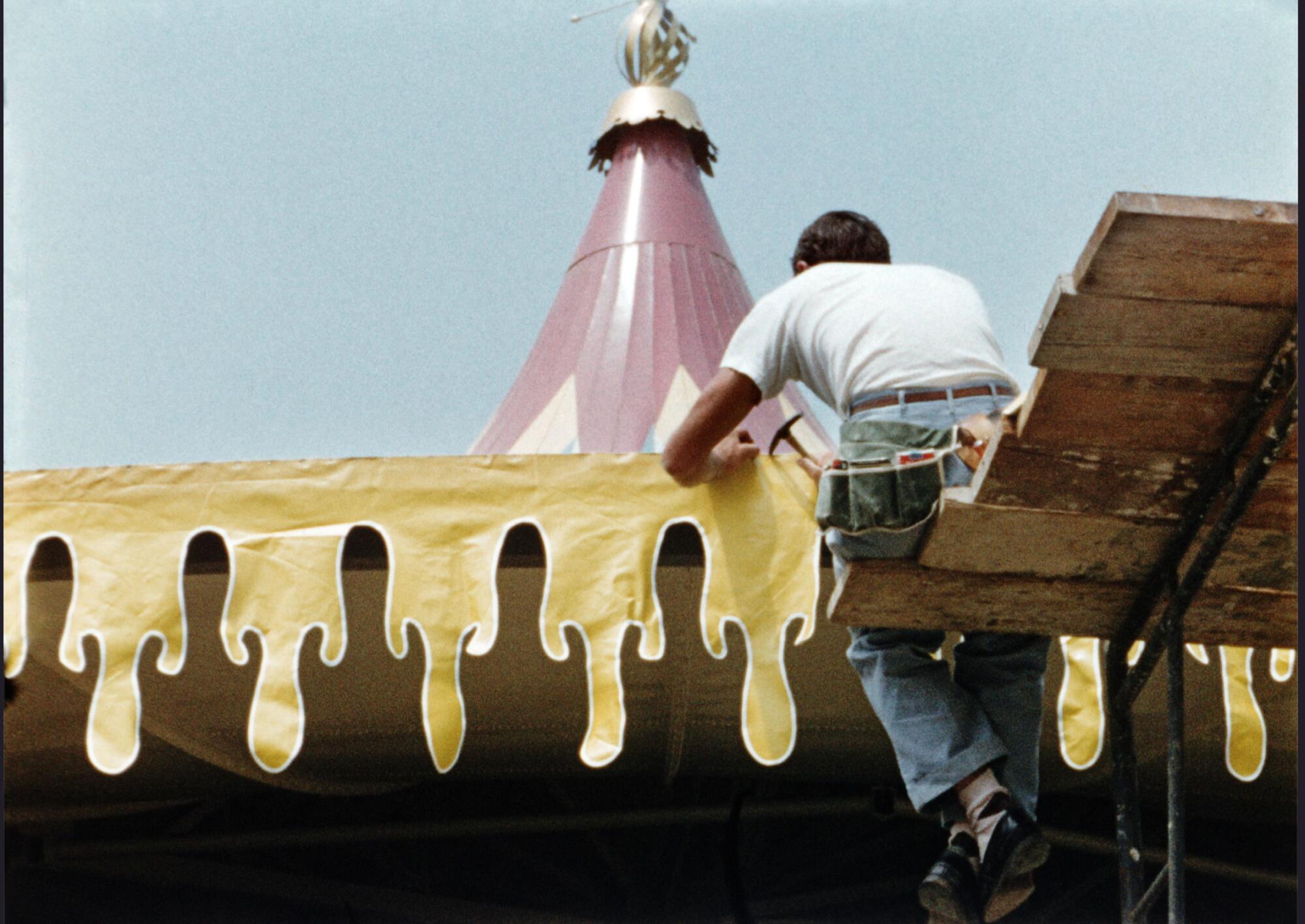 A craftsperson works on the yellow decorative trim of King Arthur Carousel in Fantasyland.