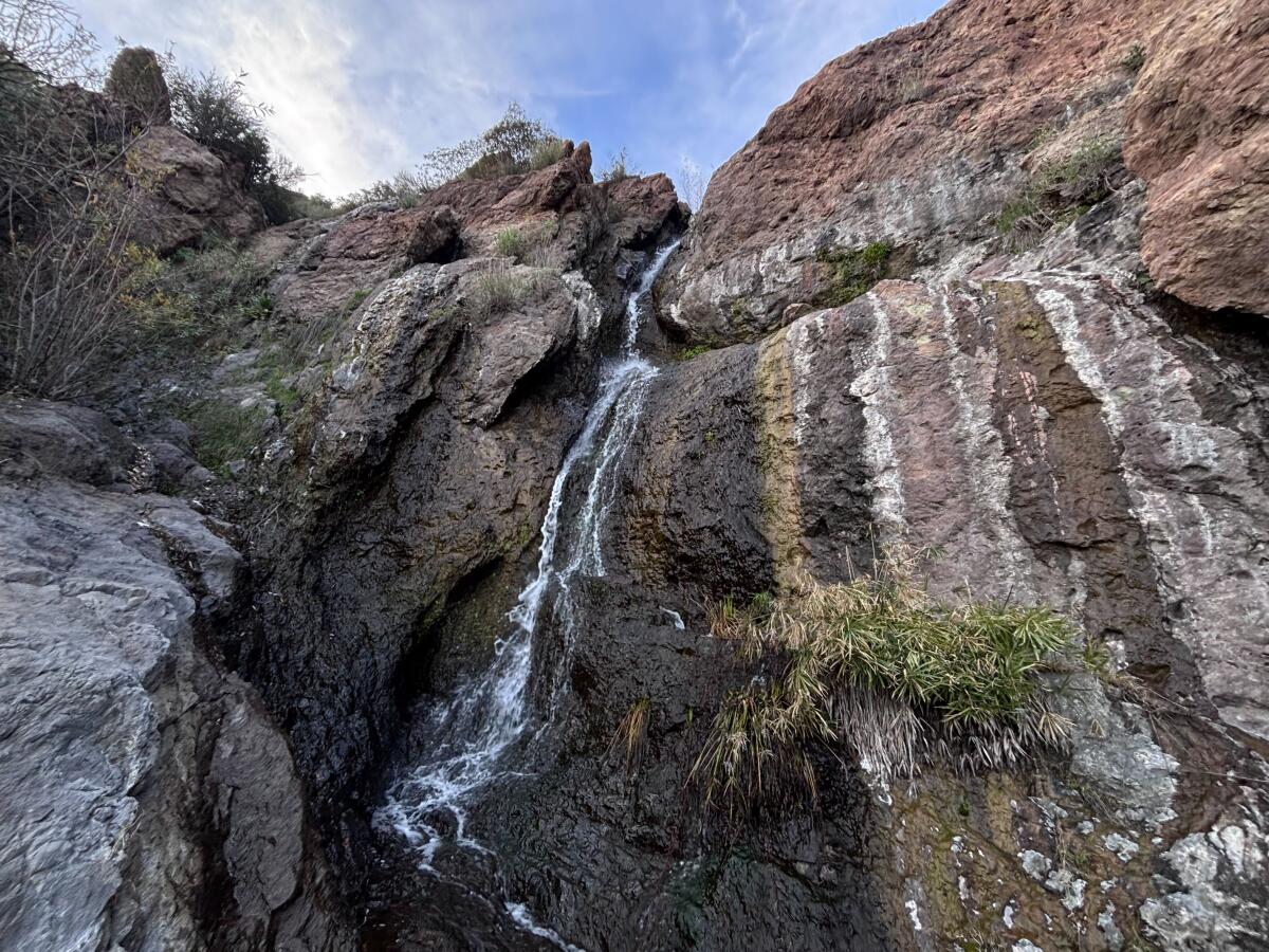 Water runs down rocks covered with moss and a white residue that makes a natural rainbow of brown, green, pink and white.