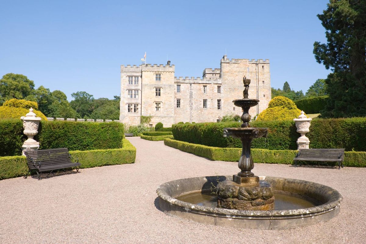 An exterior view of Chillingham castle from the back with a stone water fountain in the foreground.