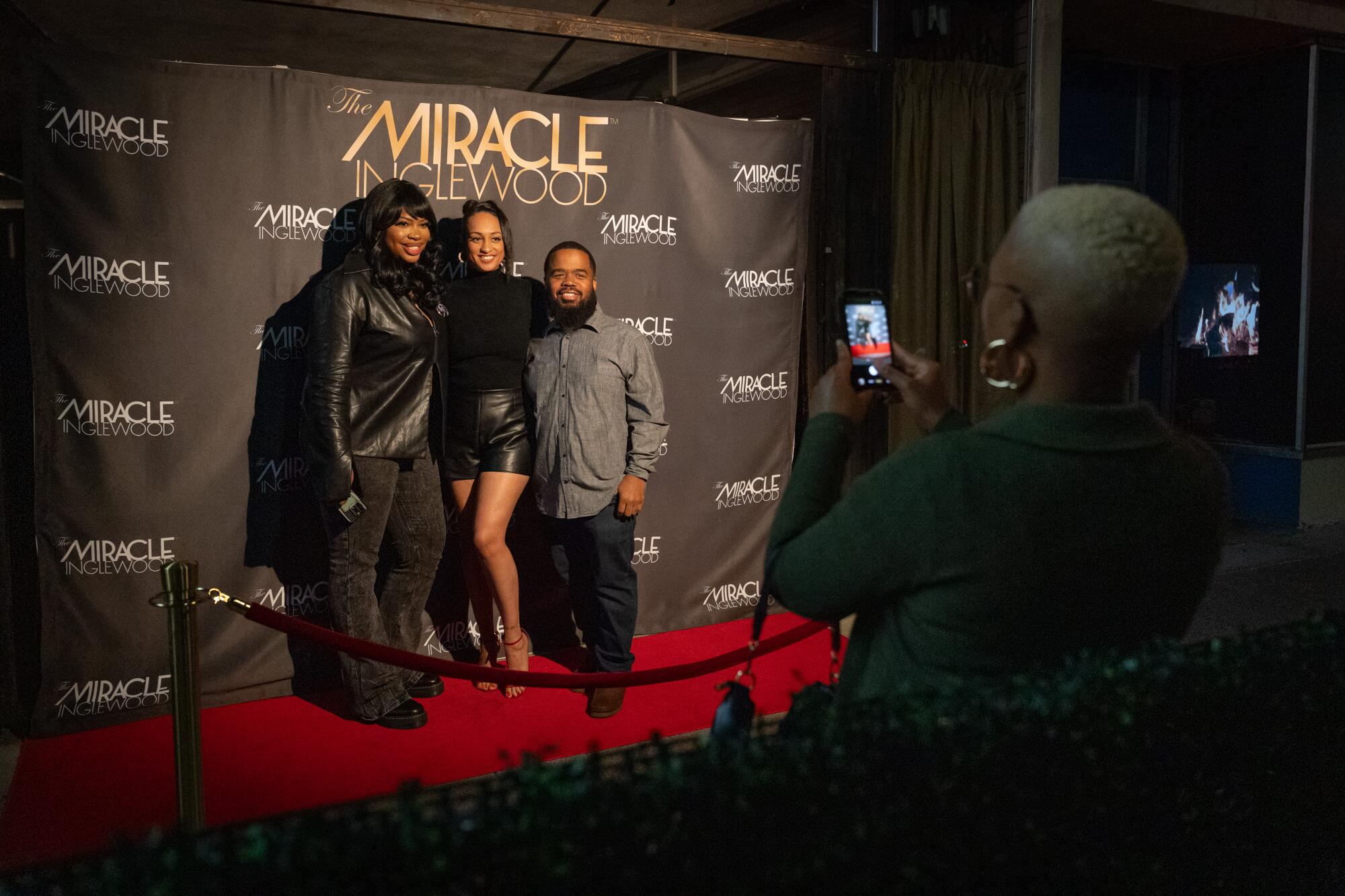 Three people take photos in front of a backdrop.
