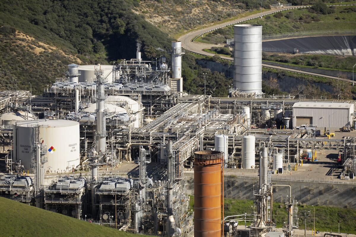 An oil production facility rises amid green hills. 