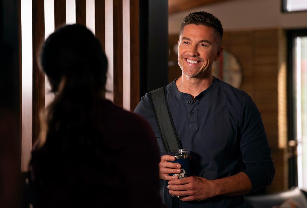 A smiling man grips a coffee tumbler with both hands