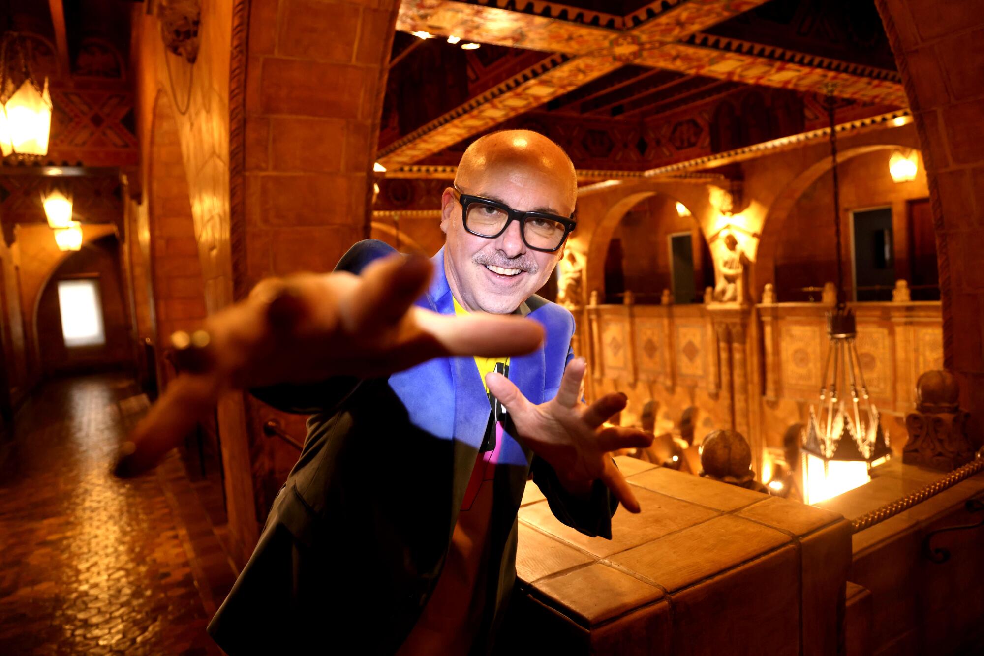 A man waves at the camera in a vintage lobby.