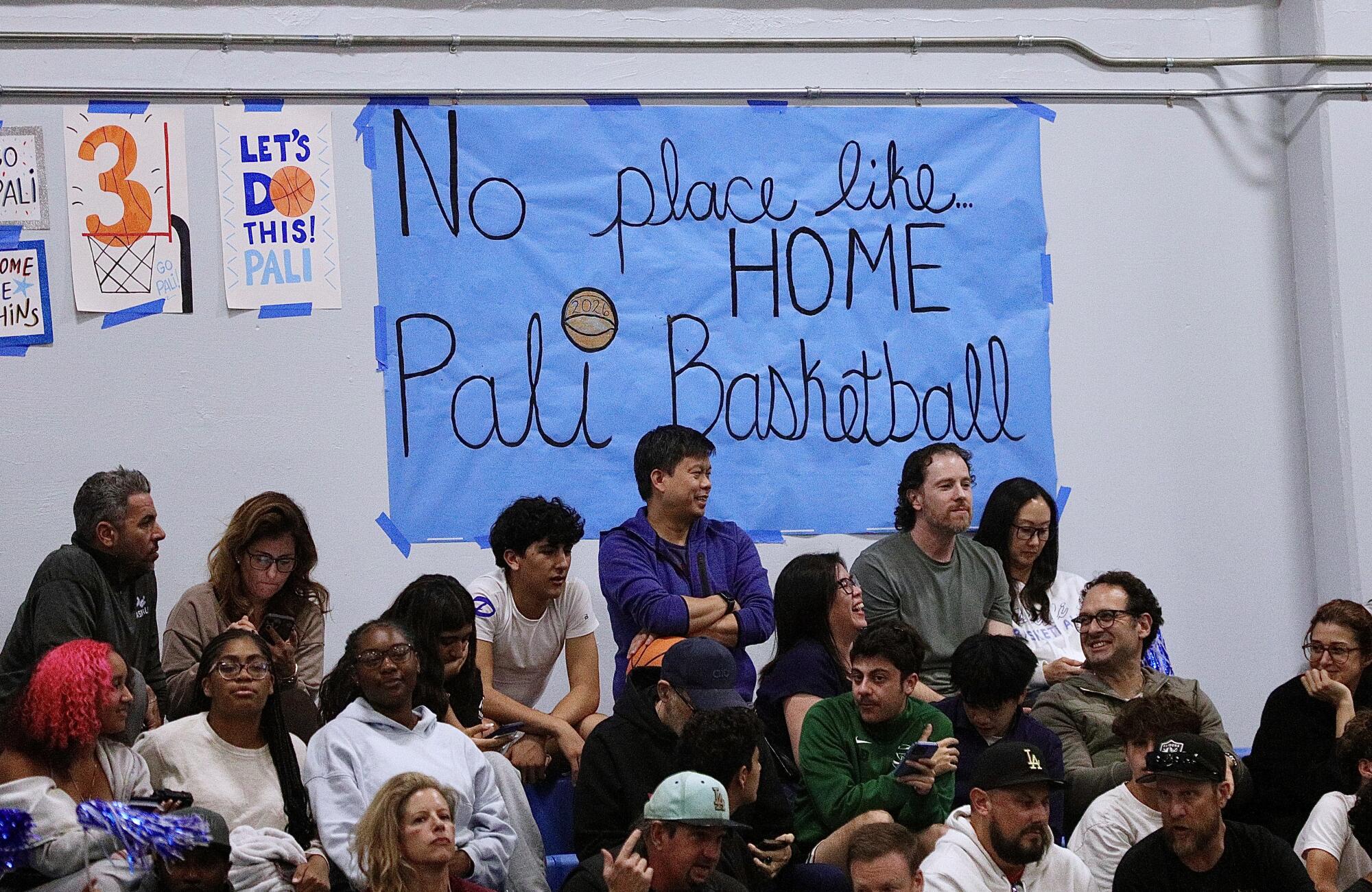 Fans sit below a sign at the Palisades High gym that says "No Place Like Home, Pali Basketball."