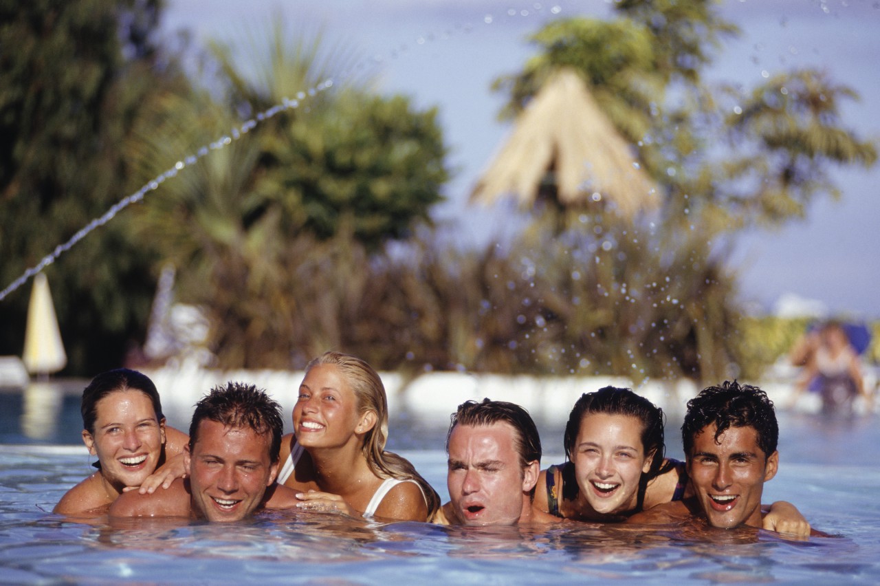 Six young people smiling in a swimming pool.
