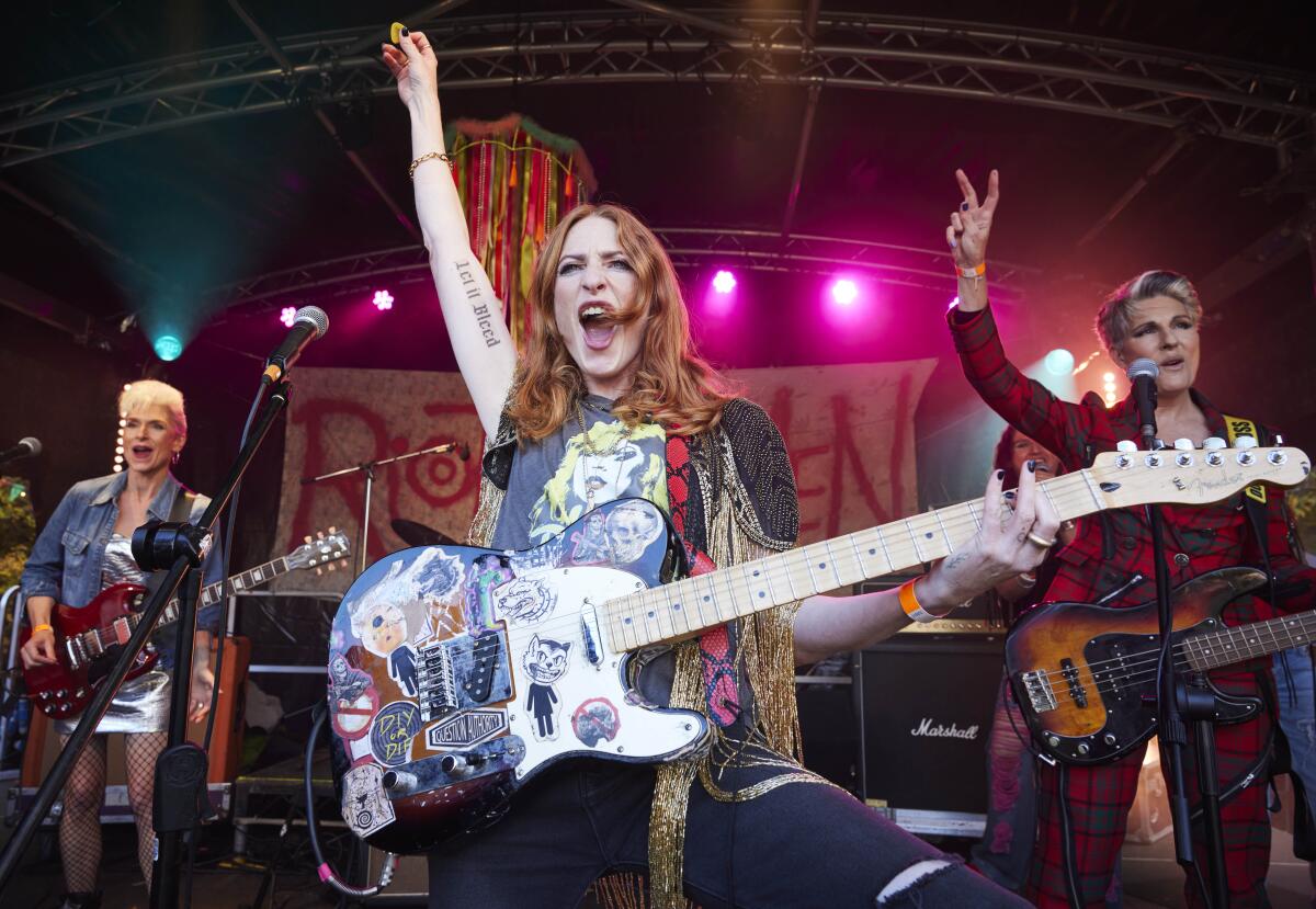 Three women holding musical instruments stand on stage.