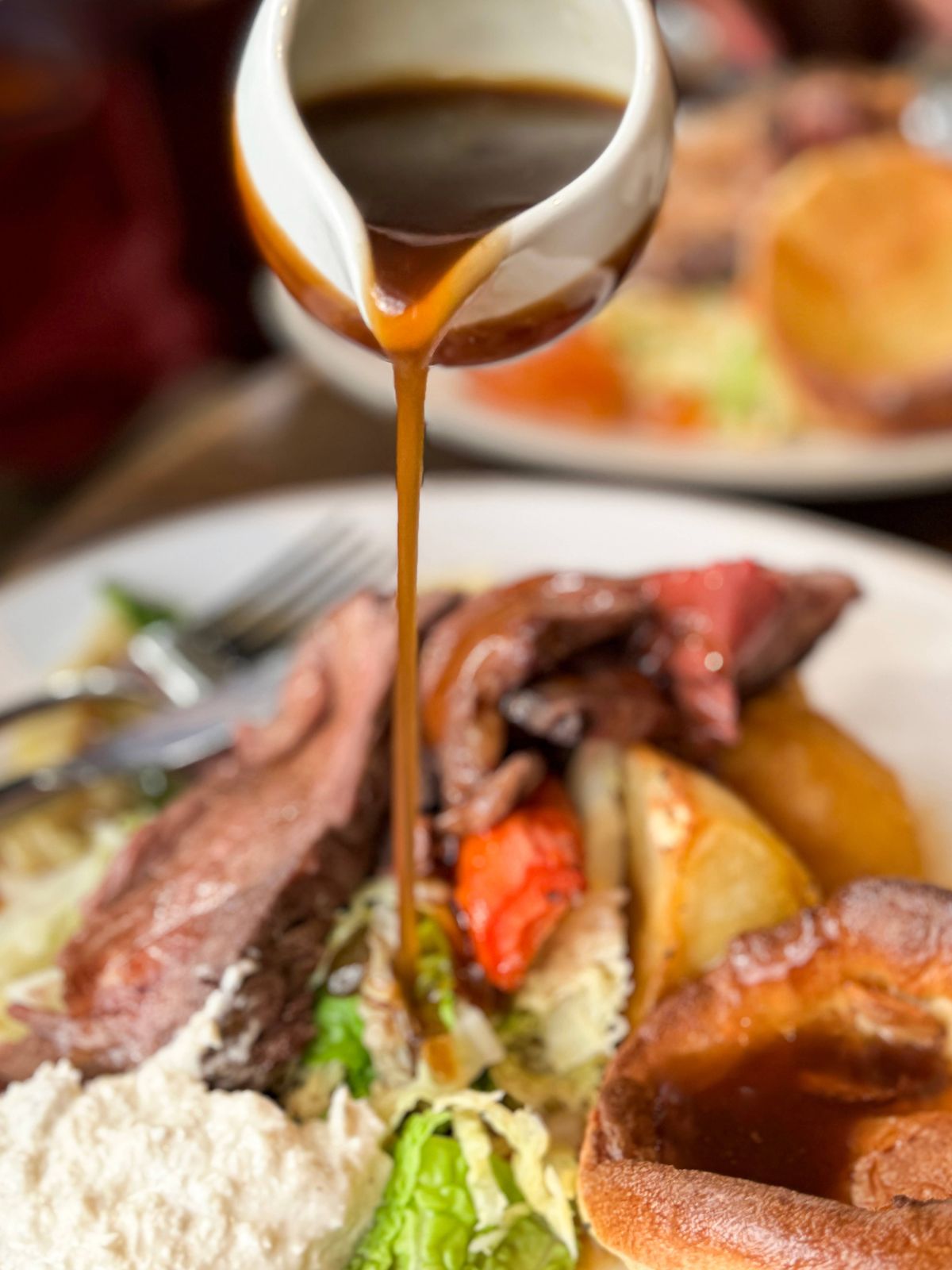 Stock photo of traditional Sunday dinner showcasing succulent roast beef, expertly cooked for maximum flavor and tenderness. Served alongside crispy roast potatoes and light, airy Yorkshire puddings, the dish is enriched with a generous pour of savory gravy. Freshly steamed cabbage and sweet carrots complete the plate