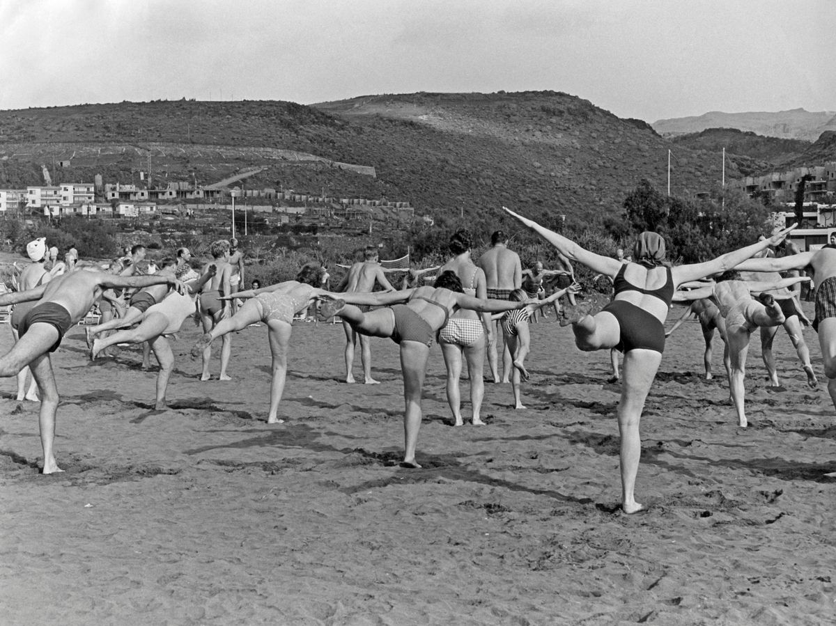 In the 1960s, a group of people are seen exercising on a beach on the Canary islands